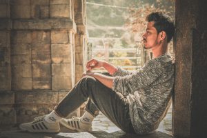 photo of man wearing gray sweater and track pants leaning on wall