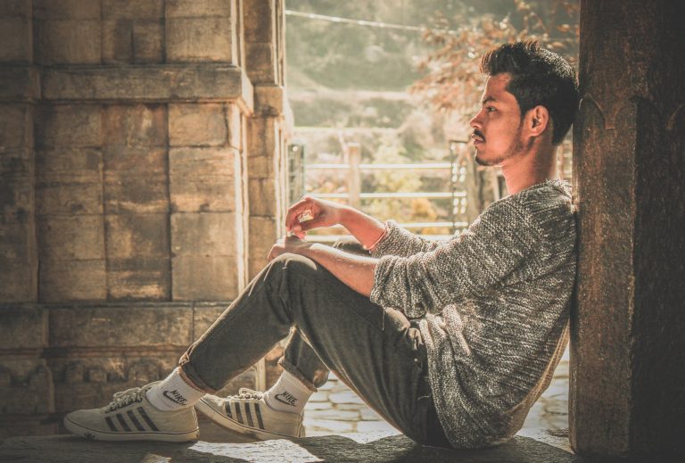photo of man wearing gray sweater and track pants leaning on wall